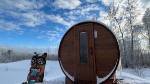 Una baita di legno con una porta circolare, un ponte di legno e un totem coperto di neve.