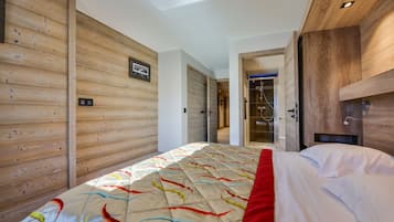 Ein modernes Hotelzimmer mit einer Holzwand, einem Bett mit farbenfroher Bettdecke und einem sichtbaren Duschbereich hinter einer offenen Tür.