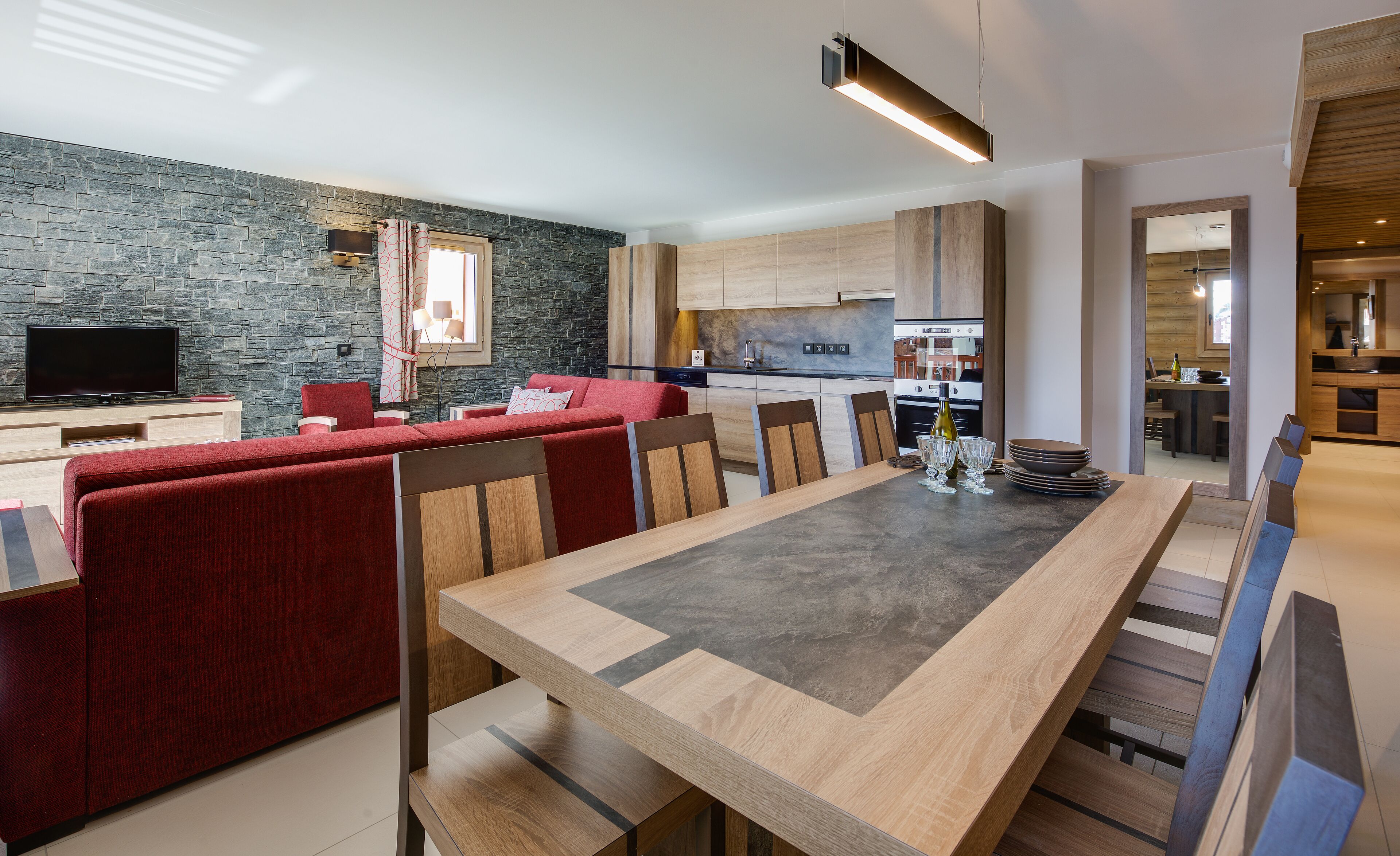 Una sala moderna con un juego de sofá rojo, una mesa de comedor de madera y una cocina al fondo.
