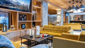 A modern interior with a stone wall, wooden shelves, and a yellow sofa. - CGH Résidence & Spa White Pearl Lodge (La Plagne-Tarentaise)