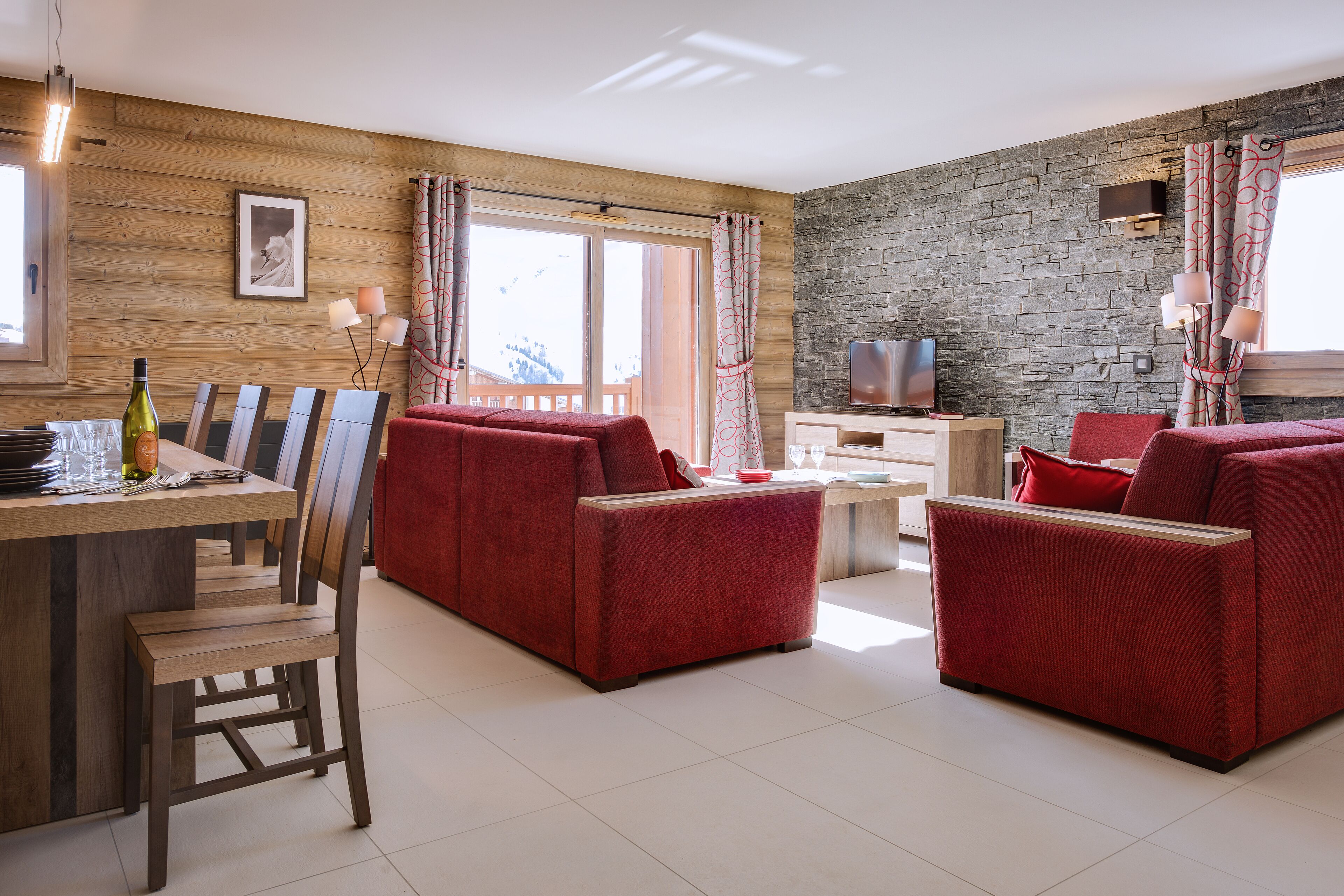 Een moderne woonkamer met een houten wand, een accentwand van steen, een televisie en een eethoek met een tafel en stoelen.