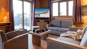 A cozy room with a wooden interior, a flat-screen TV, a sofa, a coffee table, and a teddy bear. - CGH Résidence & Spa White Pearl Lodge (La Plagne-Tarentaise)