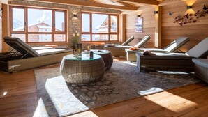 A cozy lounge area with wicker furniture, large windows, and a stone wall. - CGH Résidence & Spa White Pearl Lodge (La Plagne-Tarentaise)