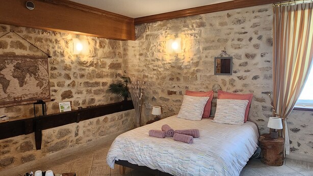 Ein Schlafzimmer mit einer Steinwand, einem Bett mit gestreifter Bettdecke, zwei Nachttischlampen und einer Karte an der Wand.