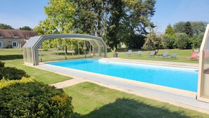 Ein Schwimmbad mit Glasüberdachung, umgeben von gepflegtem Rasen und Bäumen.