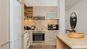 A compact kitchen with a built-in washing machine, a microwave, and a stove. - Sleek Designer Apartment in the heart of Cape Town (Cape Town)