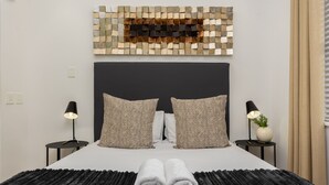 A neatly made bed with a black headboard, two bedside lamps, and a decorative wall piece above it. - Sleek Designer Apartment in the heart of Cape Town (Cape Town)