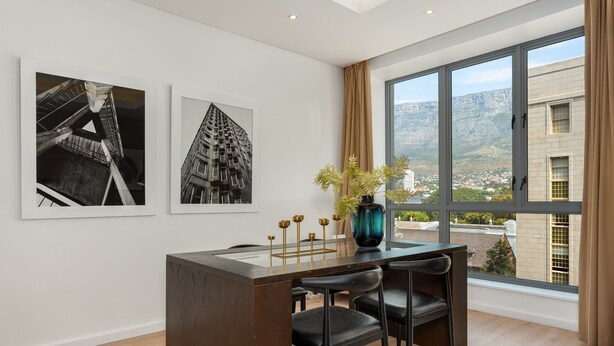 A modern room with a large window, a wooden desk, black chairs, and two black-and-white photographs on the wall. - Sleek Designer Apartment in the heart of Cape Town (Cape Town)