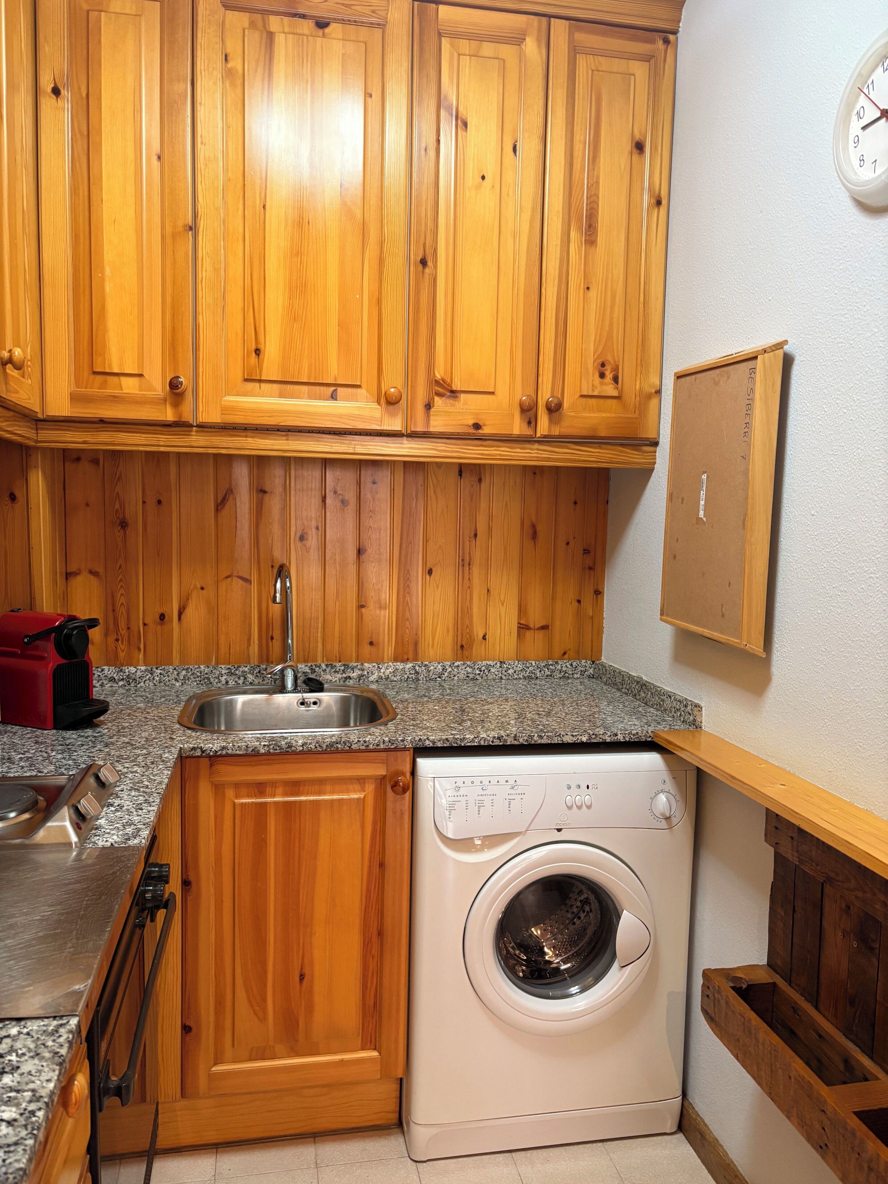 A compact kitchen with wooden cabinets, a built-in washing machine, a sink, and a red appliance.