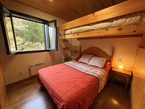 Une chambre avec un lit superposé, une fenêtre donnant sur un paysage verdoyant, une table de chevet avec une lampe et un plancher en bois.