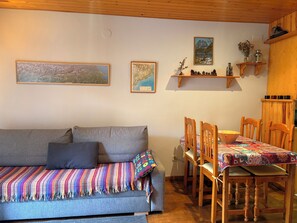 Un salon chaleureux avec un canapé gris, des chaises en bois, une table en bois et des étagères murales ornées d’objets décoratifs.