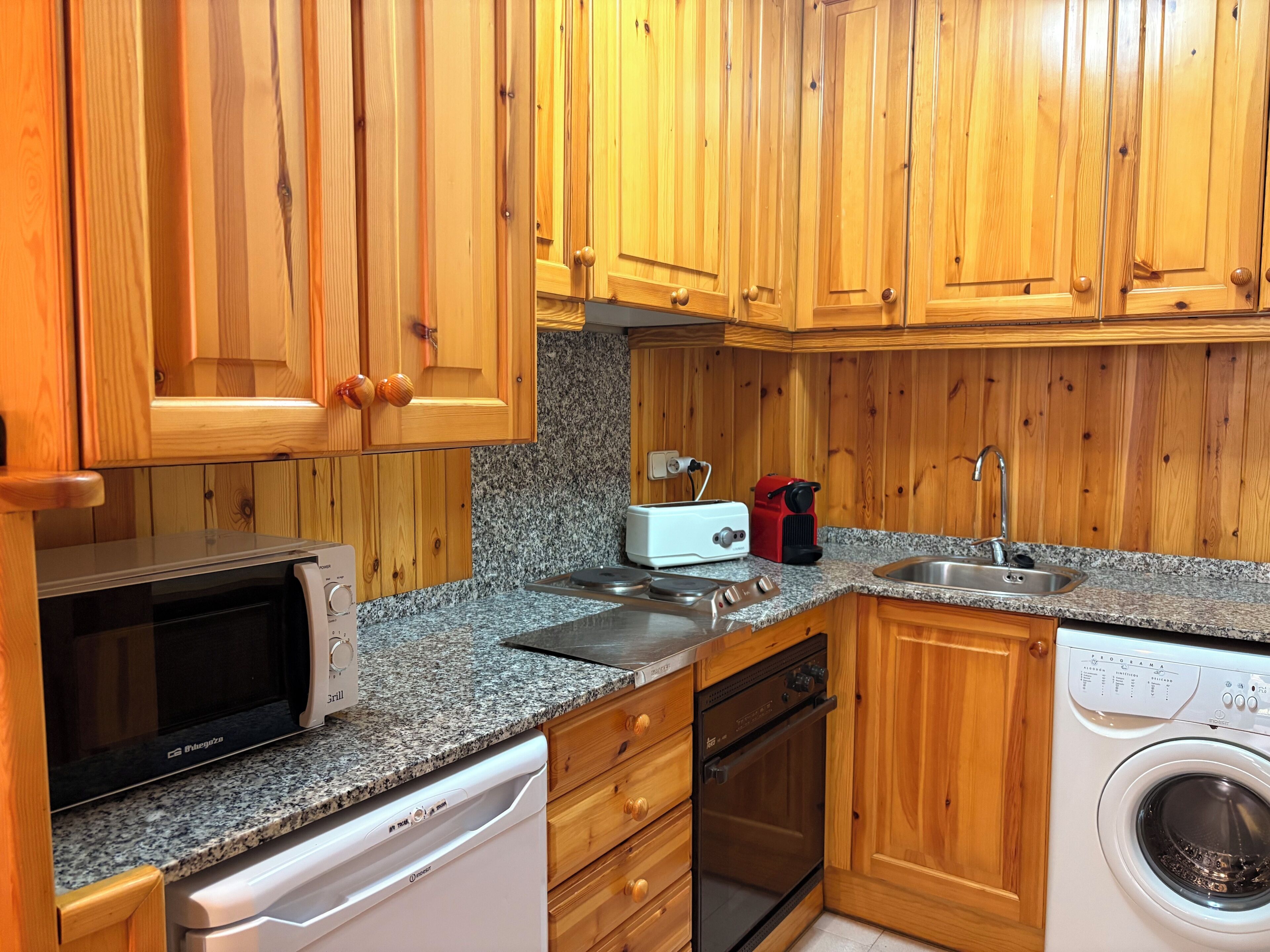 A kitchen with wooden cabinets, a microwave, a toaster, a sink, a dishwasher, and a washing machine.