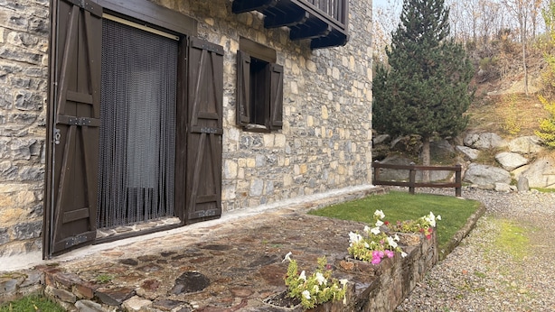 Un edificio de piedra con un balcón, una puerta de madera y un parterre de flores.