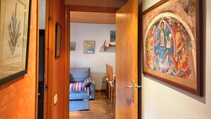 Un pasillo con puertas de madera, un sofá gris y un colorido cuadro religioso en la pared.