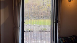Habitación con vista a través de una puerta de malla, un sofá con un cojín floral y una lámpara fijada a la pared.