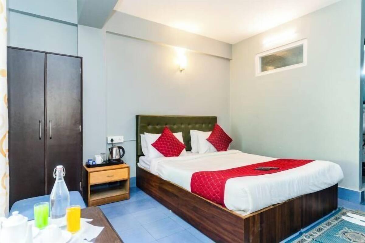 A hotel room with a bed, a nightstand, a wardrobe, and a small table with a bottle and glasses.
