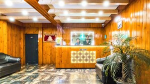 Un área de recepción con un mostrador de madera, un sofá de cuero negro y una planta en maceta.