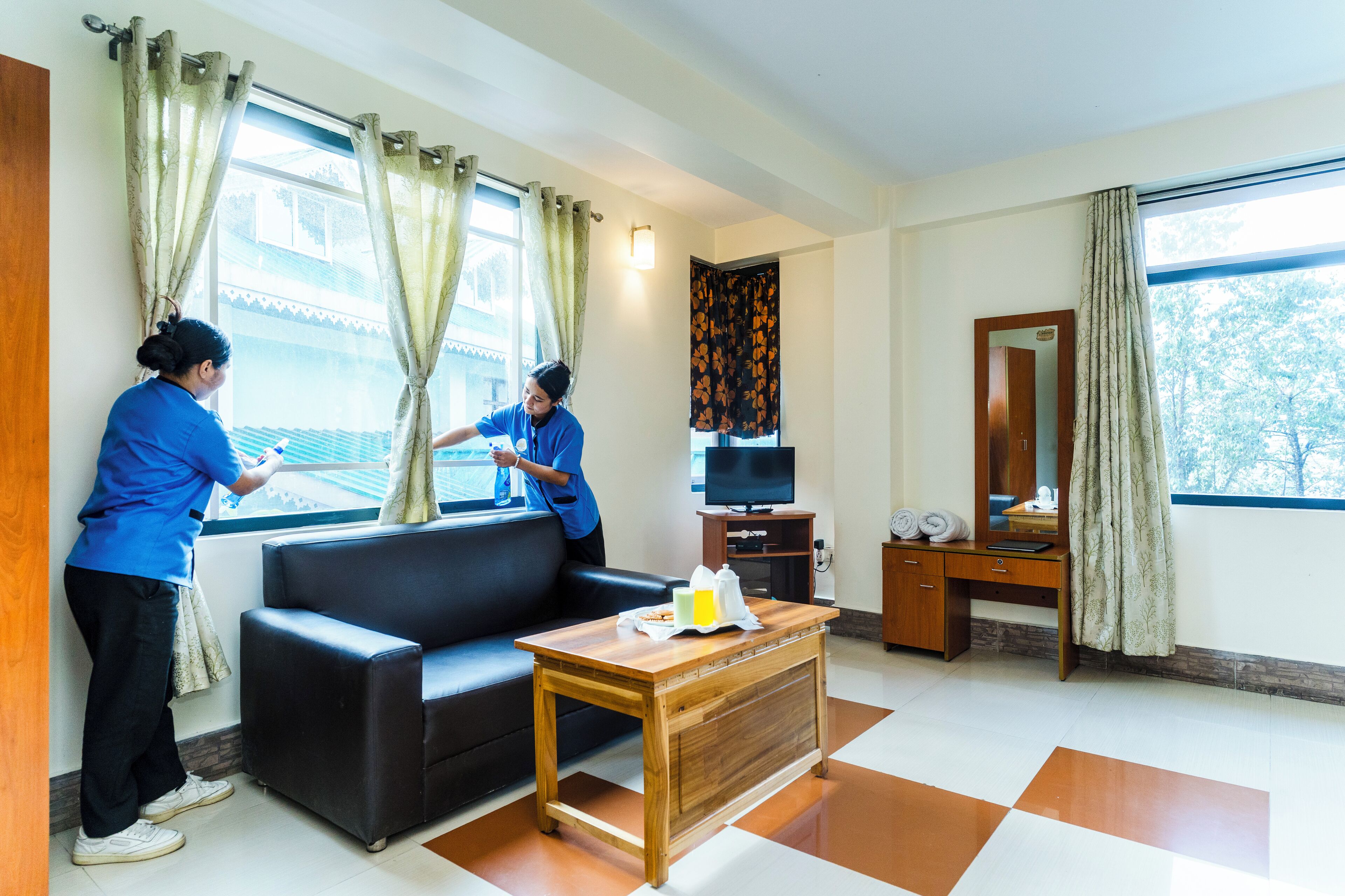 A hotel room with a black leather sofa, a wooden coffee table, a television on a stand, and a mirror on the wall.