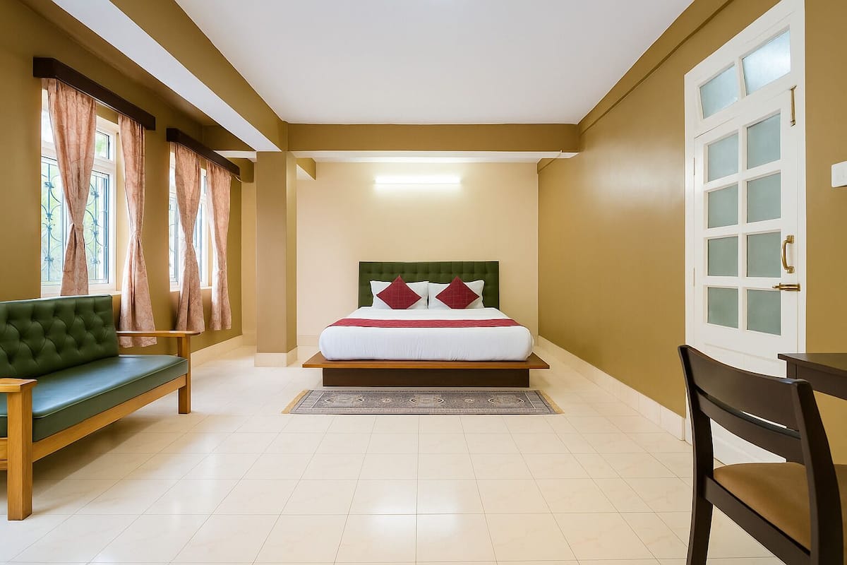 A bedroom with a bed, a green sofa, a wooden chair, and a large window with curtains.