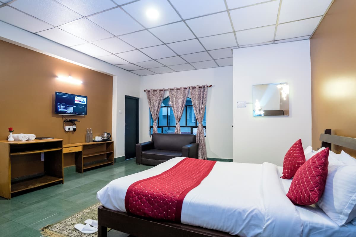 A hotel room with a bed, a desk, a chair, a TV, and a window with curtains.