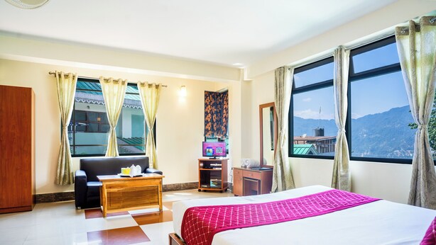 Una habitación de hotel con cama, sofá, mesa de madera, televisor y ventana con vista a la montaña.