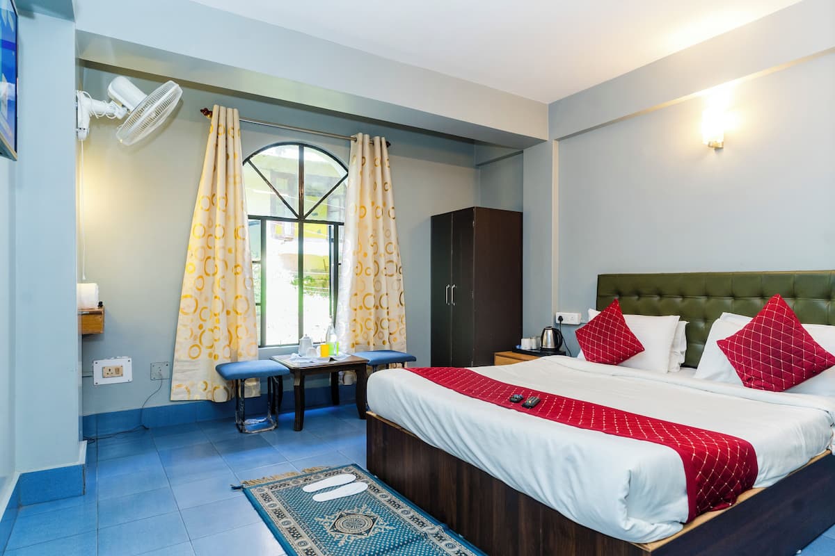 A bedroom with a bed, a desk, a chair, a wardrobe, and a window with curtains.