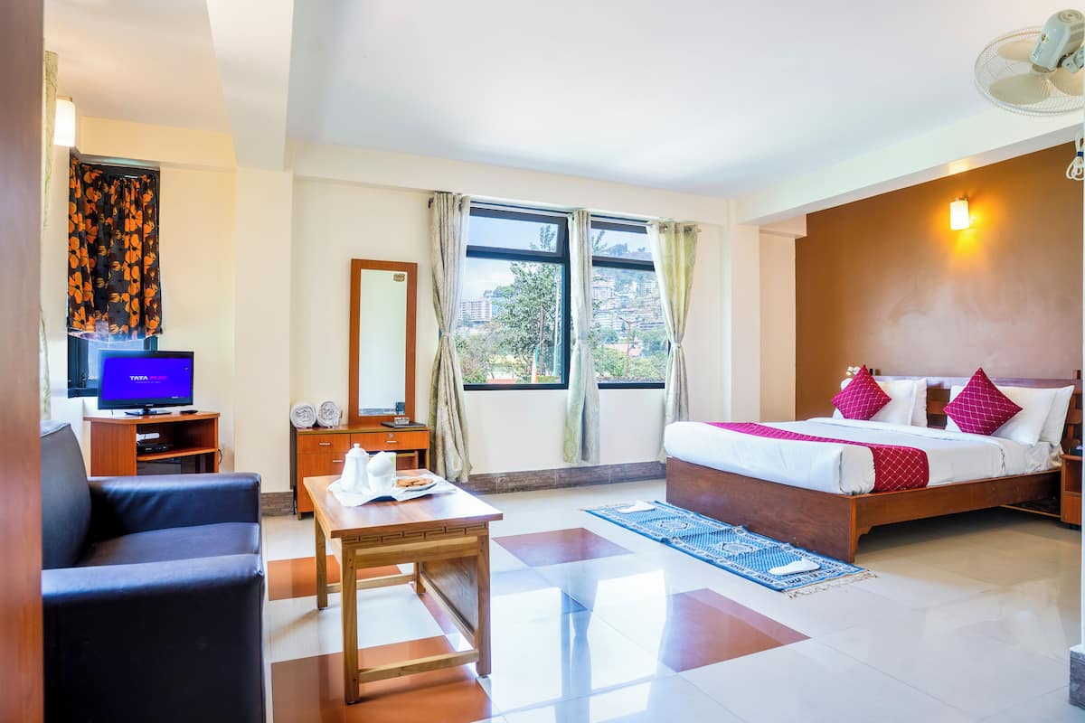 A hotel room with a bed, a desk with a computer, a sofa, and a window with curtains.