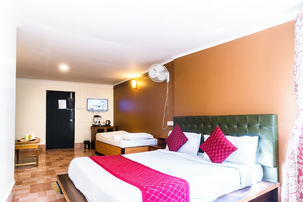 A hotel room with a large bed, a desk, a chair, a television, and a wall-mounted fan.