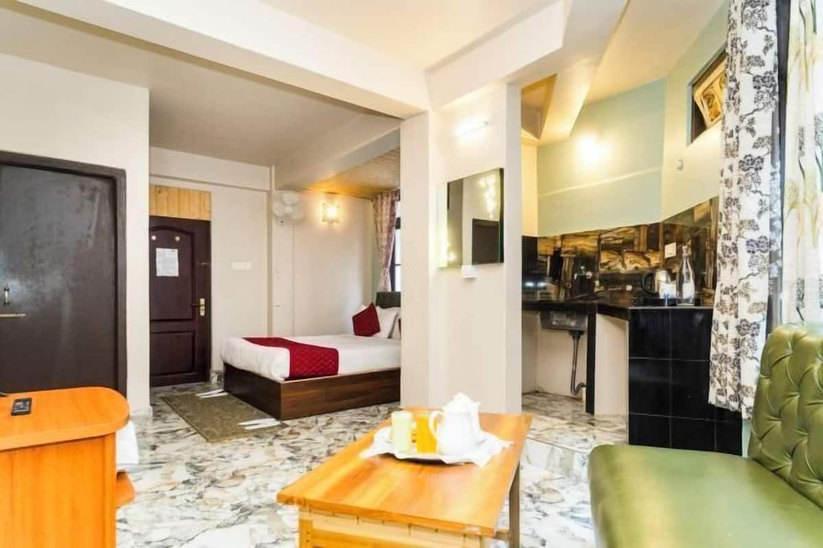 A hotel room with a bed, a small table with breakfast, a sofa, a desk, and a bathroom visible through an open door.