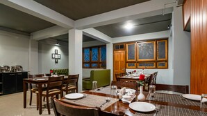 A dining area with wooden tables and chairs, a green sofa, and a kitchen area with cabinets and a countertop. - Sparrow Juniper Tree 2 min walk To Mg Marg (Gangtok)