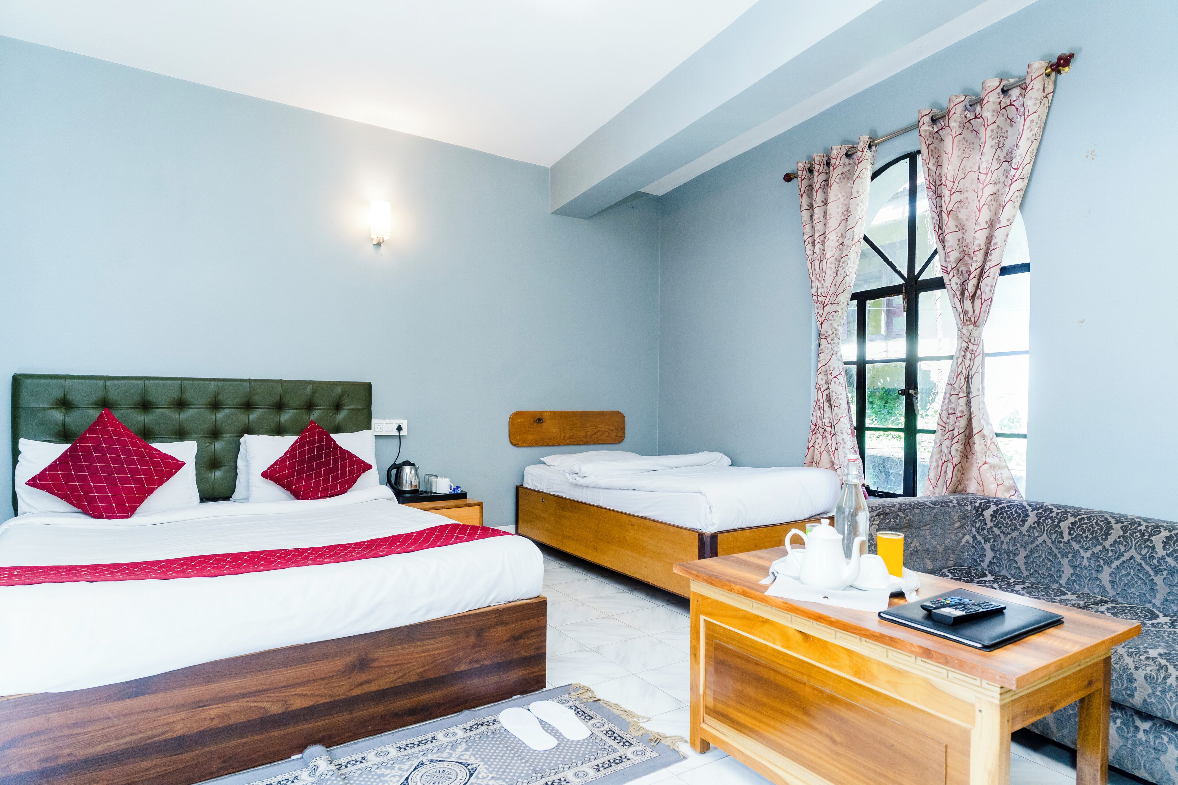 A hotel room with two beds, a sofa, a wooden table with a laptop, and a window with curtains.
