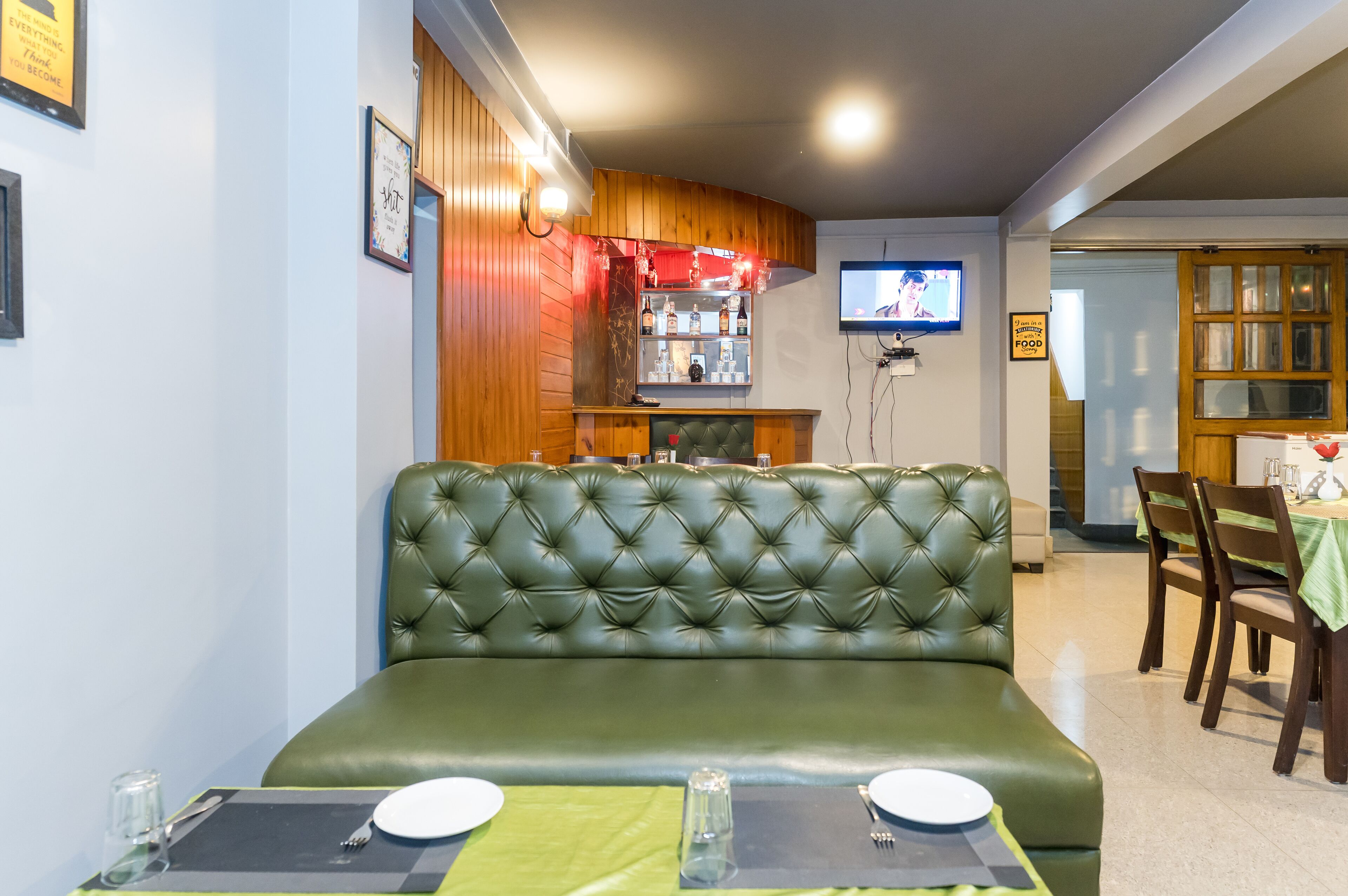 Un restaurant avec des banquettes en cuir vert, un bar où sont exposées des bouteilles et un écran de télévision.