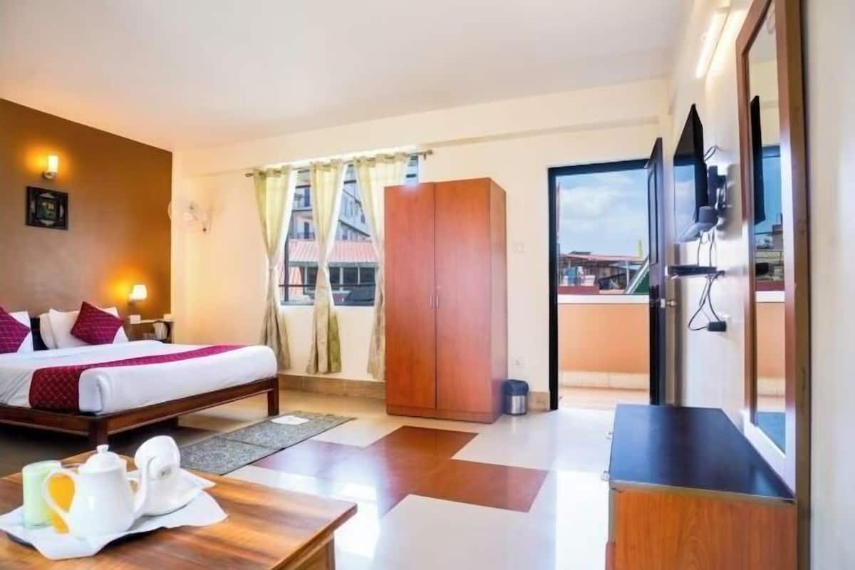 A hotel room with a bed, a wardrobe, a desk with a chair, a television, and a window with curtains.