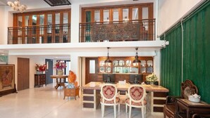Un interior espacioso de dos pisos con un comedor que incluye una mesa y sillas de madera, una cocina con armarios de vidrio y un balcón con barandilla de madera.