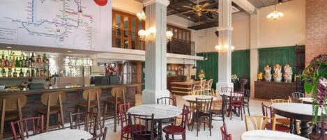 A spacious restaurant with multiple dining tables and chairs, a bar area with bottles, and a large map on the wall.