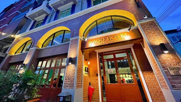 Un hotel con una entrada destacada, amplias ventanas en arco y un letrero que indica que es el AGO HOTEL.