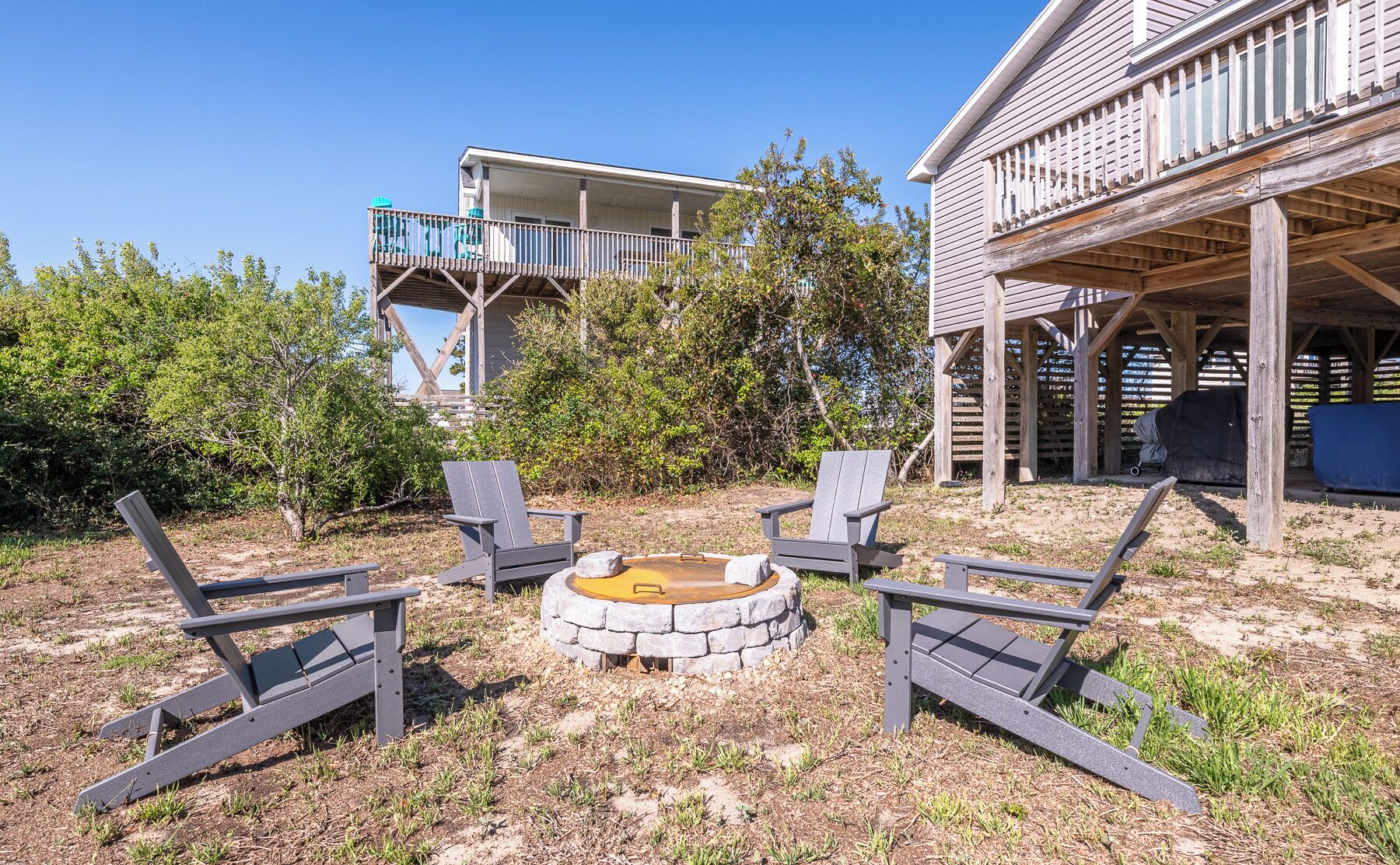 Un patio trasero con un brasero, dos sillas Adirondack y una zona de barbacoa techada.