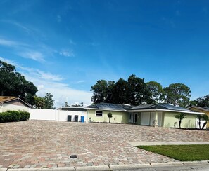Um edifício residencial com calçada pavimentada, painéis solares no telhado e uma pequena área ajardinada.