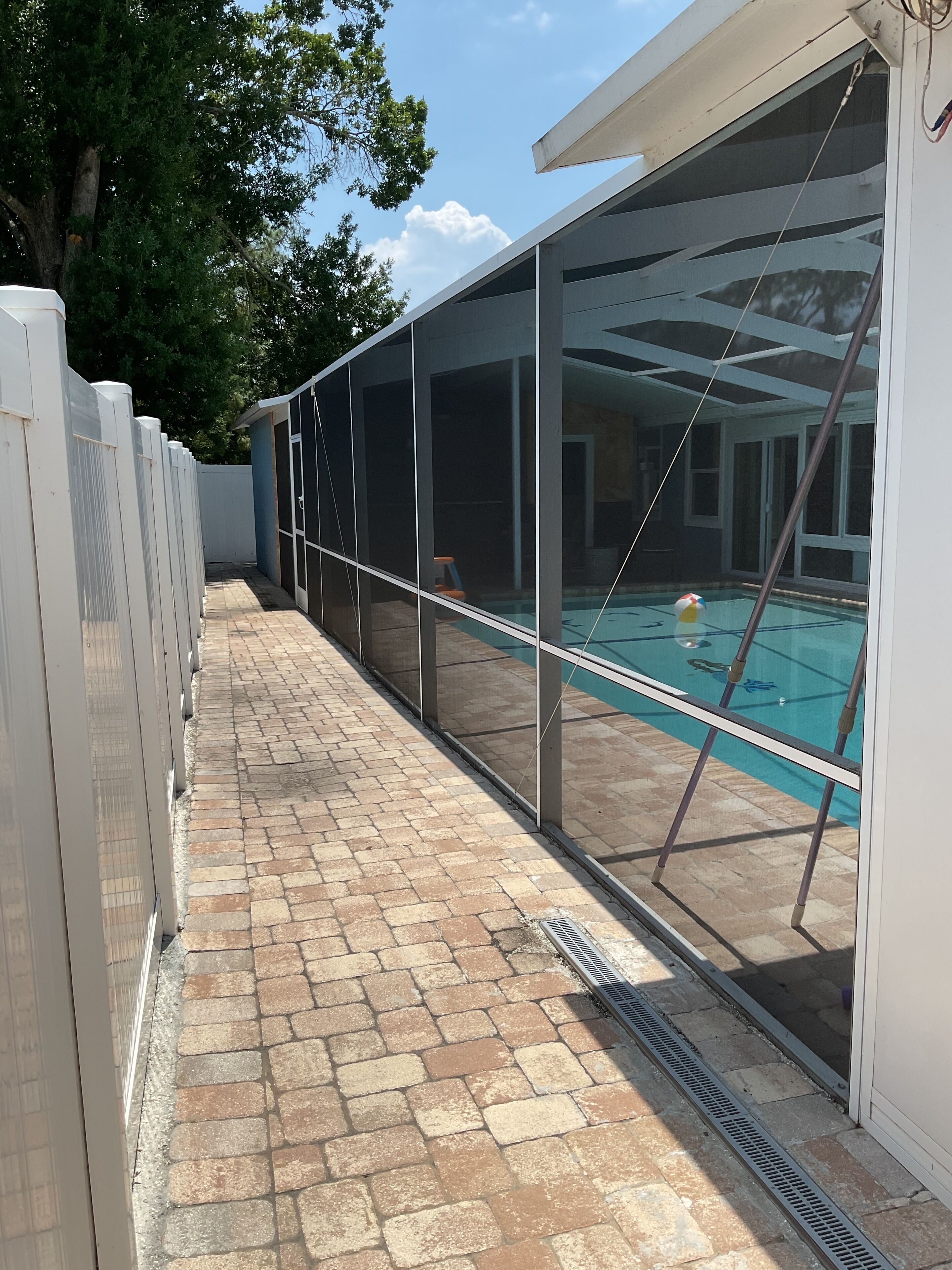 A covered outdoor swimming pool with a brick patio and a white fence.