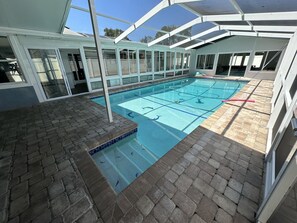 Piscina interna com água azul cristalina, emoldurada por piso de tijolos e paredes de vidro.