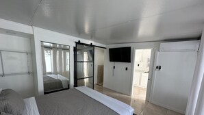 Habitación de hotel con una cama, televisor montado en la pared y una puerta corredera que da a un baño.