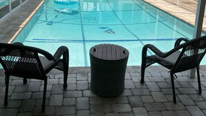 Una piscina exterior techada con dos sillones de mimbre y un bote de basura en el centro.