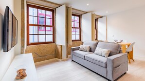 Una sala de estar moderna con un sofá gris, una mesa de centro de vidrio y un comedor con una mesa y sillas de madera.