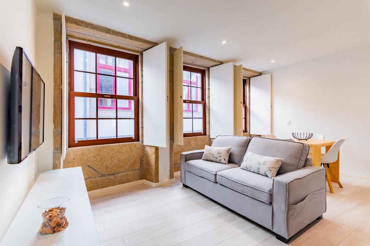 A modern living room with a grey sofa, a glass coffee table, and a dining area with a wooden table and chairs.