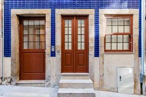 A building facade with two doors, numbered 98 and 100, and a window with a grid pattern. - Lemago São Bento (Porto)