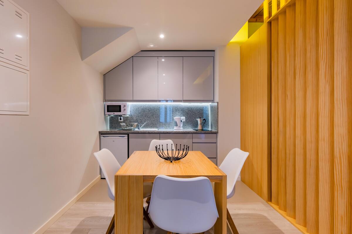 A modern kitchen with grey cabinets, a wooden dining table, and white chairs.