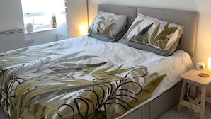 Ein modernes Schlafzimmer mit einem großen Bett, einem Nachttisch, einer Wandlampe und einem Fenster mit Blick.