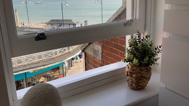 Ein Fenster mit Blick auf das Meer, ein weißes Kissen und ein gewebter Blumentopf.