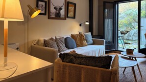 A living room with a sofa, a lamp, a table, and a view of the outdoors.