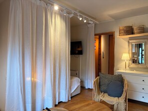 Une chambre à coucher comprenant un lit, une chaise, une commode, un miroir et un téléviseur.